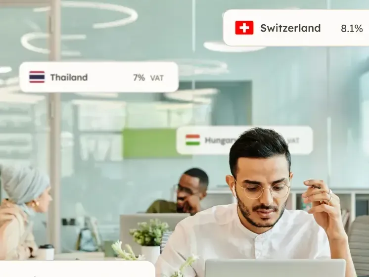 Person working at a laptop with VAT rates for Canada, Switzerland, and Thailand floating around